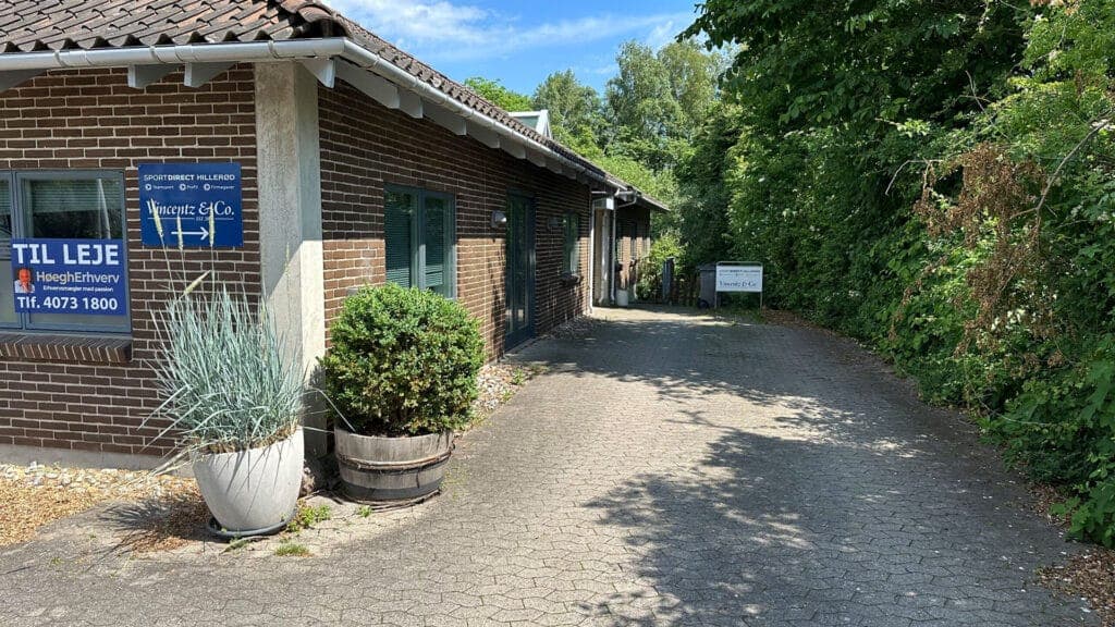 Indkørsel og egen indgang til lokalerne på Høgevej 3, med beplantning og plads til parkering